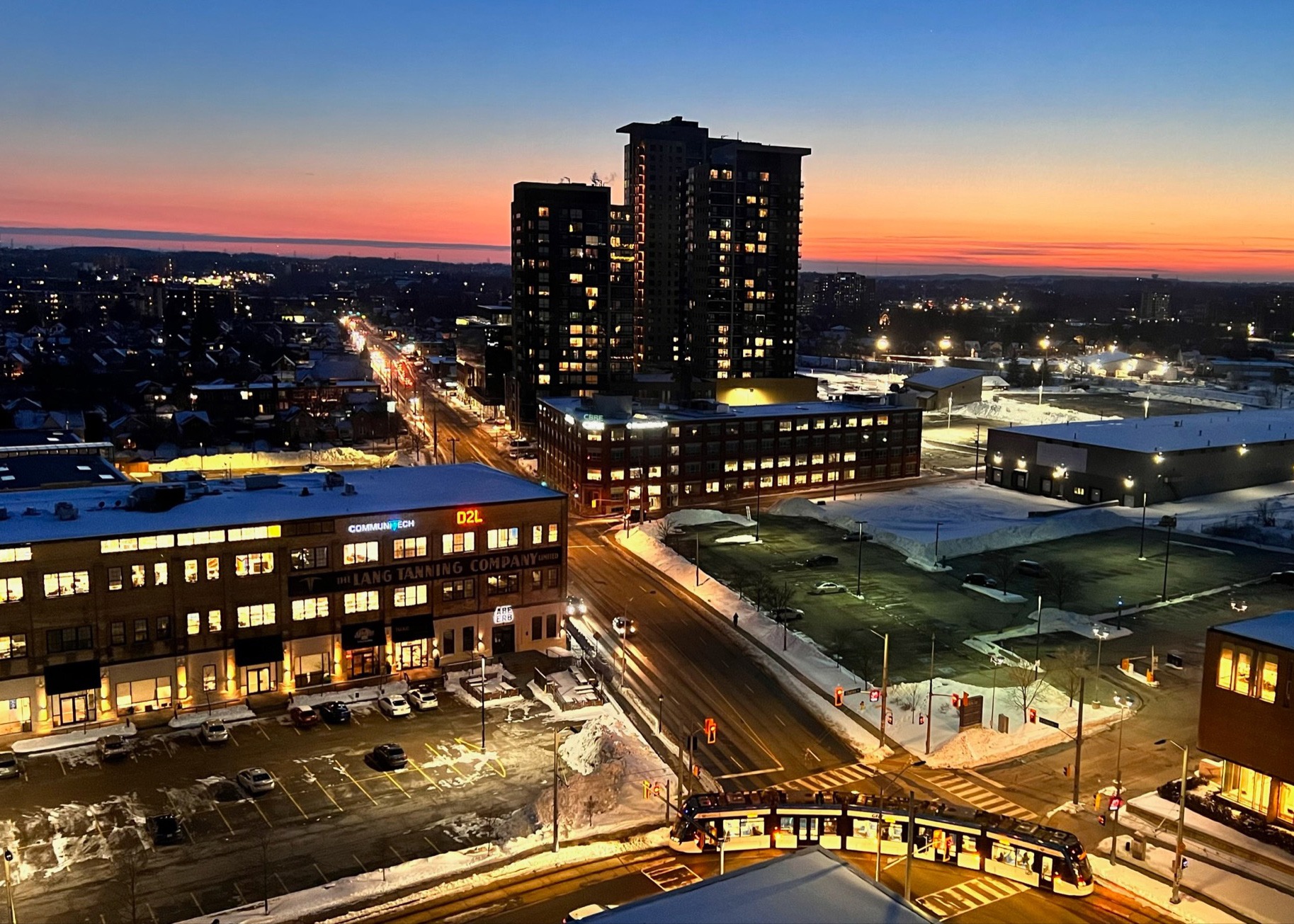 Evening aerial view of Kitchener's Innovation District. GSP Group's office at 72 Victoria Street is central to the image with three condo towers behind and the ION light rail transit passing by in the foreground.