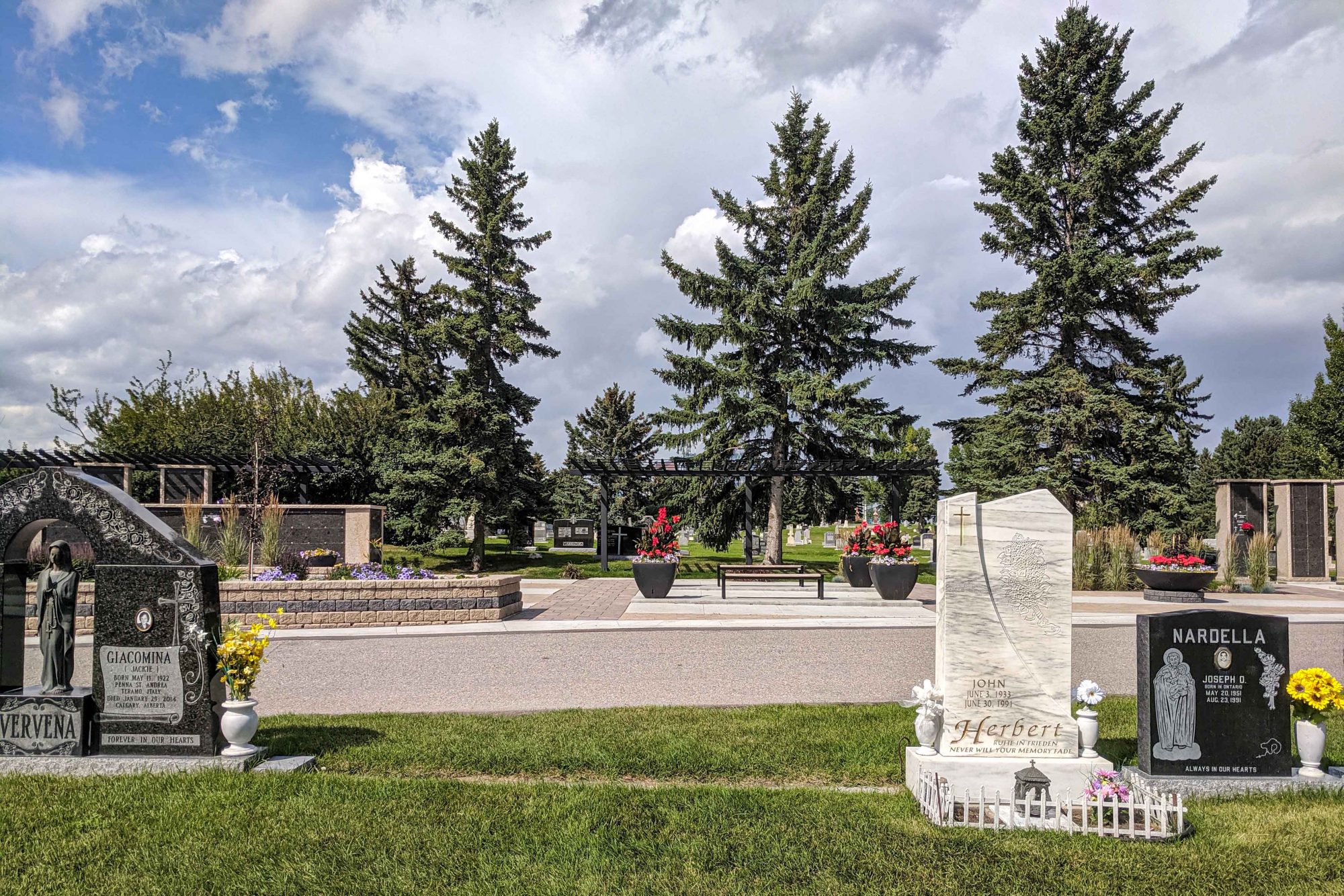 Wide view of cemetery and cremation garden with three tombstones in the foreground.